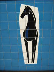 Decorative tiling with an image made up from multiple tiles; it shows a stylised head-on view of a black horse with its head turned to its right in a roughly rectangular area of white surrounded by a blue background