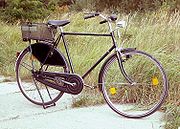 A black bicycle with nobody on it, carrying a bag, in front of a nature scene.