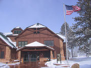 Two story wood building next to flag pole with U.S. flag waving in the wind. Snow on ground.