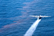 A large four propeller airplane spraying liquid over oil-sheen water