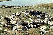 Photograph of a circular arrangement of rocks on open ground with a body of water in the background