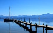 Image of a pier extending out in to a lake, with a clear sky above and mountains in the distance.