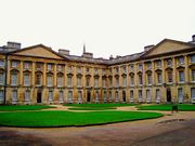 Yellow stone buildings with columns around a grassy courtyard.