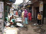 People walking on a narrow street. Shops and a stall are seen nearby.