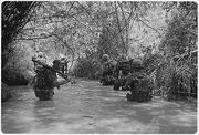 black & white photo Marines of Company H, 2nd Battalion, 4th Marine Regiment wading through a waist deep river in a jungle