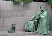 "A green statue of a man wrapped in a cloak alongside a statue of a Scottish Terrier."