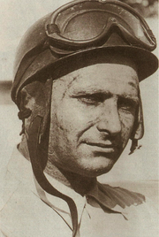 The head and shoulders of a man in his 40's, wearing a helmet with goggles placed on top of it, and a lightly-coloured shirt