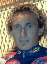 Close up of a curly-haired blond man in his mid-twenties wearing a pink and purple cycling jersey