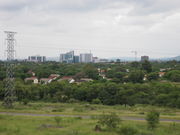 A skyline picture of Gaborone with a field, forest, and low-lying houses in the foreground and buildings along the horizon.