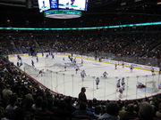 Slightly elevated view of an active ice rink. Players on one team wear mostly red and white uniforms, while the others are outfitted predominately in blue.