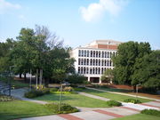 A sidewalk surrounded by landscaped green space in the foreground with a four-story white concrete building in the background