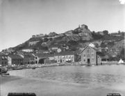 Modest buildings  along the water's edge are guarded by a fortress on the hill above.