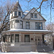 gabled two-story house with corner turret and wrap-around porch under a clear sky