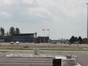 A building on a clear day. It is situated amongst considerable asphalt, with trees in the bacground. Two flag poles are in front of the building, an Ontario and Canada flag. The building is designed with particular attention to obscure angles.