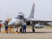 A light fighter aircraft on the ground surrounded by two men who are maintaining it.