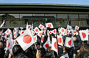 A group of people wave Japanese flags at a palace.