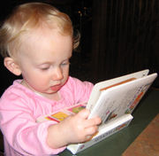 A baby sits a rug on the floor surrounded by toys. He stares down at a cloth book in his hands in a posture of interest and concentration.