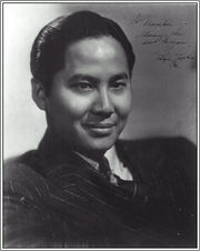 Head and shoulders publicity shot of a young, smiling man, short hair slicked back and wearing a suit and tie.