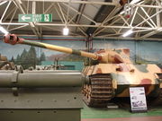 A frontal view of a large tank in a museum, painted pale yellow with some green and rust-brown blotches. Its curved-faced turret is turned to the left and the long gun overhangs the side by several meters.