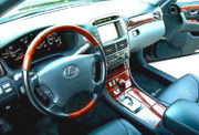 Automobile front interior, driver side, with dashboard navigation screen, wood steering wheel and console.