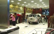 Car showroom with an SUV and customers, along with a metal waterfall fixture and paintings.