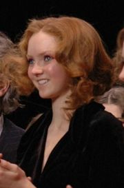 Head and shoulders shot of curly red haired, blue-eyed young woman dressed in black.