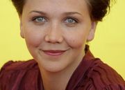 A close-up shot of a woman's face. She has brown hair and light blue eyes, and is wearing a red top.