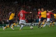 Wayne Rooney (in red) is shaping to kick the ball with an Arsenal player (in yellow) on either side of him. Cristiano Ronaldo, Carlos Tévez (both Manchester United) and Kolo Touré (Arsenal) are looking on in the background.