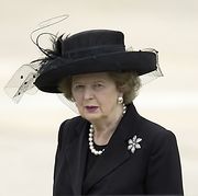 Thatcher in a black suit and hat, with a solid white background.