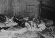 Black and white photograph of an eviscerated human body lying on a bed. The face is mutilated.