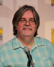  A man in glasses and a plaid shirt sits in front of a microphone.