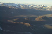  In the foreground is a landscape of dull brown mounds and undulations, behind which are snow-covered mountain peaks.