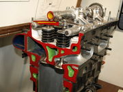 A sectioned, parallel valve, aircraft engine cylinder head is shown with colour-coded internal details. Coolant passage ways are painted green; the valves, valve springs, camshaft and rocker arms are also shown.