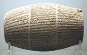 Front view of a barrel-shaped clay cylinder covered in cuneiform script written around the circumference in three columns of horizontal script.