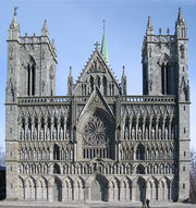 A Romanesque church with Gothic pointed arches. Two rectangular towers separated by a pitched roof entrance hall. The ornate facade is heavily articulated with repeated arches, most of them framing statues.