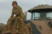 A woman wearing a camouflaged military uniform sitting on the bonnet of a camouflaged truck