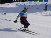 A woman sitting on sit-skis, she is pushing herself with two poles