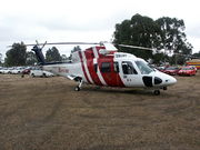 A helicopter painted red and white at rest on grass. Cars are parked in the background.