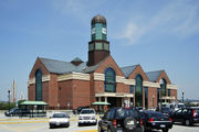 Three-story brick building with three gables on roof; large clock tower made of green glass seen at center of left gable.