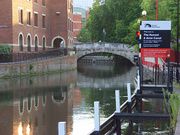 Canal passing under an arched bridge. To the left are buildings. On the right is a sign saying Welcome to the Kennet and Avon Canal.