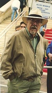 Photo of the director Robert Altman in his mid-60s, wearing a goatee, glasses, a wide-brimmed white hat and a jacket and looking directly into the camera.