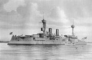 A large gray warship with two tall masts and two thin smoke stacks sits motionless offshore