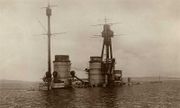 The top of a warship juts out of calm water after it had been sunk