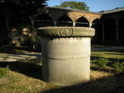 A stout cylindrical column in a courtyard in front of palatial arches of Islamic style