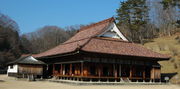 Wooden building with a hip-and-gable style roof  and an open veranda surrounding the building.