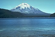 Conical mountain with snow near the top as seen from a lake