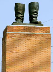 a tan brick pedestal supporting a pair of bronze statue boots with nothing attached