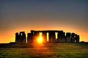 Sun shining through row of upright standing stones with other stones horizontally on the top.