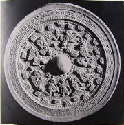 A round object with an inscription  in Chinese characters around the outer part and figurative relief in  the middle.