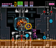 A video game screenshot. A person in a powered exoskeleton fires a projectile at a brain in a glass-protected chamber.